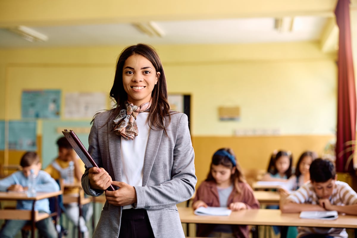 Happy elementary school teacher in the classroom looking at camera.